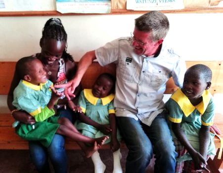 Patricia und Achim von BlackAndWhite sitzen lachend auf einer Holzbank mit 3 Kids, ebenfalls lachend mit Behinderungen